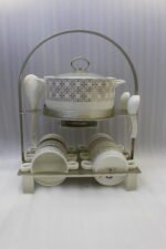 Luxury white and gold geometric pattern ceramic soup tureen set with matching mugs, spoons, and silver metallic rack on a marble kitchen counter