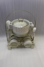 Luxury white and gold geometric pattern ceramic soup tureen set with matching mugs, spoons, and silver metallic rack on a marble kitchen counter
