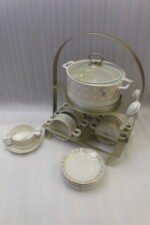 Luxury white and gold geometric pattern ceramic soup tureen set with matching mugs, spoons, and silver metallic rack on a marble kitchen counter