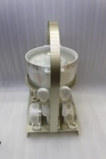 White ceramic soup tureen with glass lid, matching dual-handled soup bowls, saucers, and spoons organized on a two-tier gold metal rack.