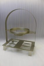 White ceramic soup tureen with glass lid, matching dual-handled soup bowls, saucers, and spoons organized on a two-tier gold metal rack.