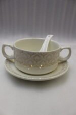 Luxury ceramic soup tureen set featuring a patterned soup pot, soup bowls with handles, matching saucers, spoons, and a gold metal stand on a wooden dining table.