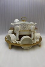 Luxury white ceramic soup tureen set with gold leaf pattern on a metal buffet burner stand with matching bowls and spoons.