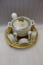 Luxury white ceramic soup tureen set with gold leaf pattern on a metal buffet burner stand with matching bowls and spoons.