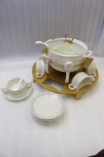 Luxury white ceramic soup tureen set with gold leaf pattern on a metal buffet burner stand with matching bowls and spoons.