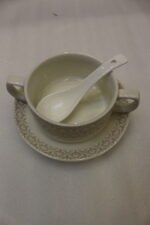 Luxury white ceramic soup tureen set with gold leaf pattern on a metal buffet burner stand with matching bowls and spoons.