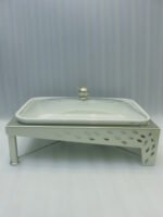 Three ceramic single buffet dishes with clear glass lids and champagne gold stainless steel warming stands displayed on a marble kitchen counter.