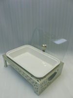 Three ceramic single buffet dishes with clear glass lids and champagne gold stainless steel warming stands displayed on a marble kitchen counter.