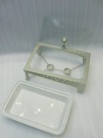 Three ceramic single buffet dishes with clear glass lids and champagne gold stainless steel warming stands displayed on a marble kitchen counter.