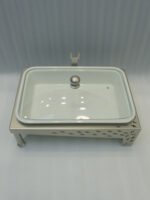 Three rectangular ceramic single buffet dishes with clear glass lids set in champagne gold stands on a kitchen marble countertop.