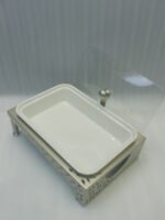 Three rectangular ceramic single buffet dishes with clear glass lids set in champagne gold stands on a kitchen marble countertop.