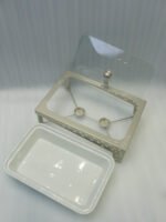 Three rectangular ceramic single buffet dishes with clear glass lids set in champagne gold stands on a kitchen marble countertop.