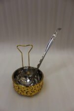 Luxury gold and stainless steel round chafing dish buffet server with a glass dome lid suspended on a gold frame, matching ladle, and buffet burner on a kitchen counter.