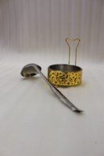 Luxury gold and stainless steel round chafing dish buffet server with a glass dome lid suspended on a gold frame, matching ladle, and buffet burner on a kitchen counter.