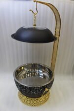 One More luxury matte black and gold hanging lid buffet chafing dish with stainless steel pan on a marble kitchen counter.