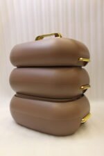Three stacked matte taupe One More insulated hot pots with gold handles on a white kitchen countertop.