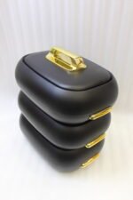 Three matte black insulated hot pot food containers with gold lid handles resting on a marble kitchen countertop.