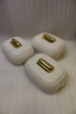 Three stacked off-white insulated hot pot casseroles with metallic gold handles sitting on a marble kitchen countertop.