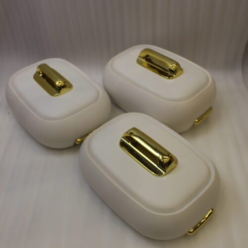 Three stacked off-white insulated hot pot casseroles with metallic gold handles sitting on a marble kitchen countertop.