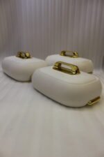 Three stacked off-white insulated hot pot casseroles with metallic gold handles sitting on a marble kitchen countertop.