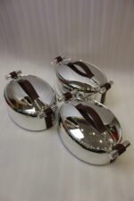Set of three One More polished stainless steel oval hot pots with brown leather handles in 2L, 2.5L, and 3L sizes on a wooden tabletop.