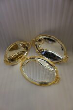 Set of three silver mirrored oval serving trays with floral etchings and textured gold handles on a marble countertop.