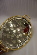 Set of three silver mirrored oval serving trays with floral etchings and textured gold handles on a marble countertop.