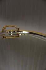 Set of three silver mirrored oval serving trays with floral etchings and textured gold handles on a marble countertop.