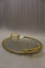 Set of three silver mirrored oval serving trays with floral etchings and textured gold handles on a marble countertop.