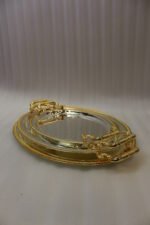 Set of three silver mirrored oval serving trays with floral etchings and textured gold handles on a marble countertop.