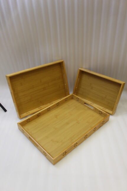 Three-piece natural wooden serving tray set with decorative floral side cutouts displayed on a marble kitchen counter.