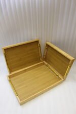 Set of three rectangular natural wood serving trays with gold metal handles displayed on a white marble kitchen countertop.