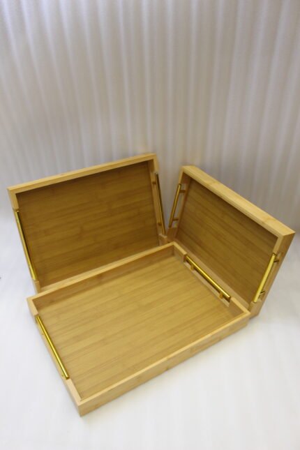 Set of three rectangular natural wood serving trays with gold metal handles displayed on a white marble kitchen countertop.