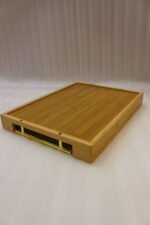 Set of three rectangular natural wood serving trays with gold metal handles displayed on a white marble kitchen countertop.
