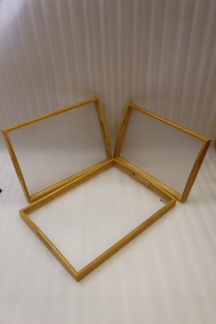Set of three natural wood nesting serving trays with cutout handles and smooth white inner bases displayed on a kitchen marble countertop.