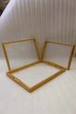 Set of three natural wood nesting serving trays with cutout handles and smooth white inner bases displayed on a kitchen marble countertop.