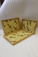 Set of three light wood rectangular serving trays featuring a golden wheat sheath pattern and built-in side handles displayed on a kitchen counter.