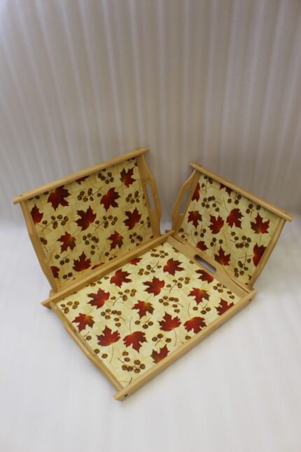 Set of three rectangular wooden serving trays featuring a red maple leaf and berry print displayed on a light kitchen countertop.