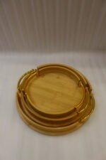 Set of 3 nesting round bamboo wooden serving trays with stylish gold metal handles on a white countertop.