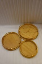 Set of 3 nesting round bamboo wooden serving trays with stylish gold metal handles on a white countertop.