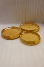 Set of 3 nesting round bamboo wooden serving trays with stylish gold metal handles on a white countertop.