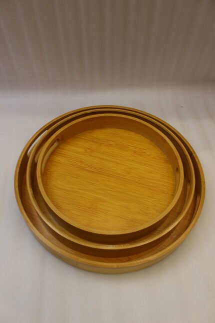 Three round natural wooden serving trays with cutout handles arranged on a marble kitchen countertop.