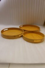 Three round natural wooden serving trays with cutout handles arranged on a marble kitchen countertop.