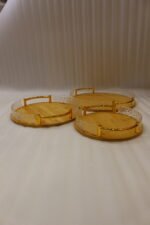 Set of three round wooden nesting serving trays with curved gold handles and clear textured glass rims stacked on a grey marble kitchen countertop.
