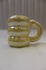 Four iridescent chubby ceramic mugs in pastel pink, yellow, mint green, and white displayed on a marble countertop.