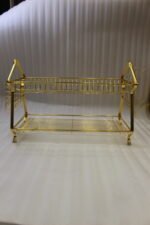 2 tier luxury gold metal dish drying rack with utensil basket, glass holder hooks, and clear drip tray on a kitchen countertop next to a faucet.