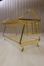 2 tier luxury gold metal dish drying rack with utensil basket, glass holder hooks, and clear drip tray on a kitchen countertop next to a faucet.