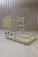 Cream two-tier metal dish drying rack with side utensil holder and drain tray on a kitchen countertop next to a sink.