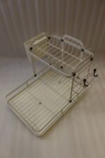 Cream two-tier metal dish drying rack with side utensil holder and drain tray on a kitchen countertop next to a sink.