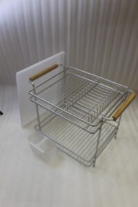 Two-tier silver dish drying rack with wooden side handles, hanging utensil holders, and a plastic drip tray on a kitchen countertop.